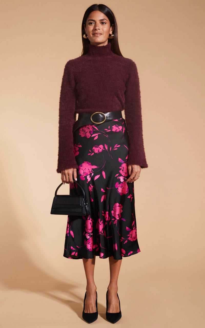 Model facing forward wearing the Lotus Skirt In Pink On Black Floral and the Poppy Jumper In Chocolate with black heels.