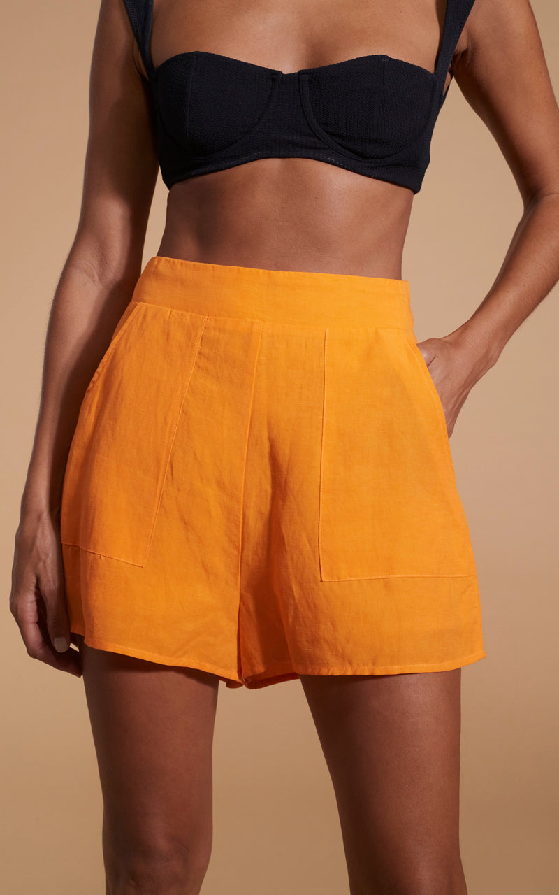 close up of Dancing Leopard model wearing Lola Linen Shorts In Orange posed with hand in pocket