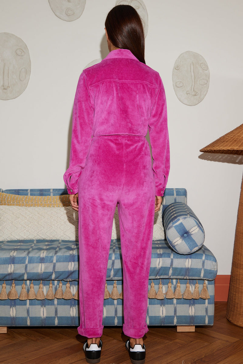 Female model faces backwards. She wears a Dancing Leopard bright pink velour jumpsuit.