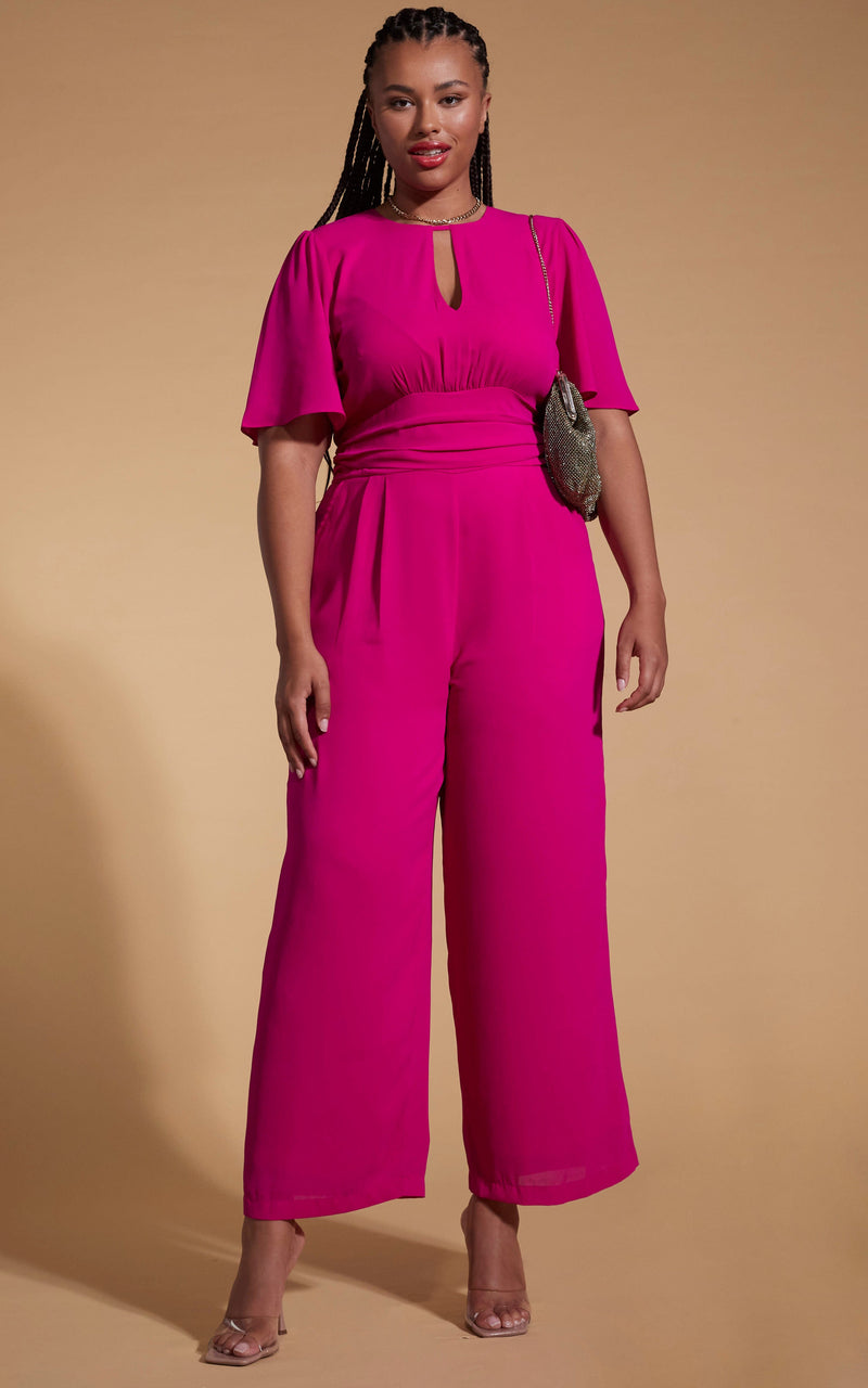 Model faces forward wearing a pink dancing leopard jumpsuit with a gold clutch bag.