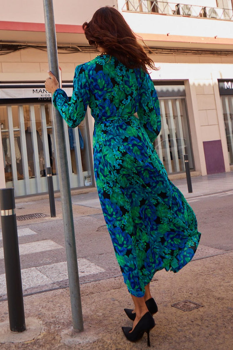 Female model is facing backwards. She wears a Dancing Leopard blue and green floral wrap dress and black high heels.