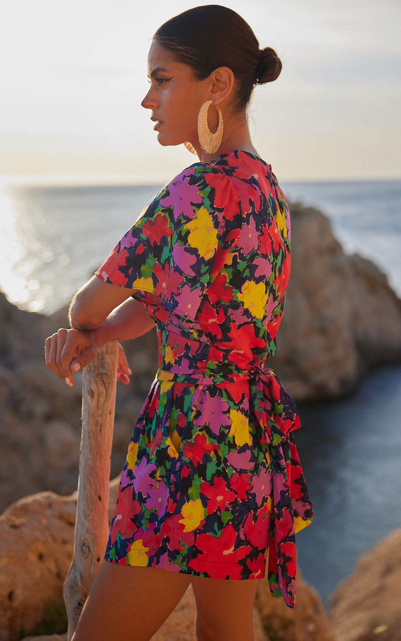 A female model faces backwards. She wears a Dancing Leopard colourful, floral printed playsuit.