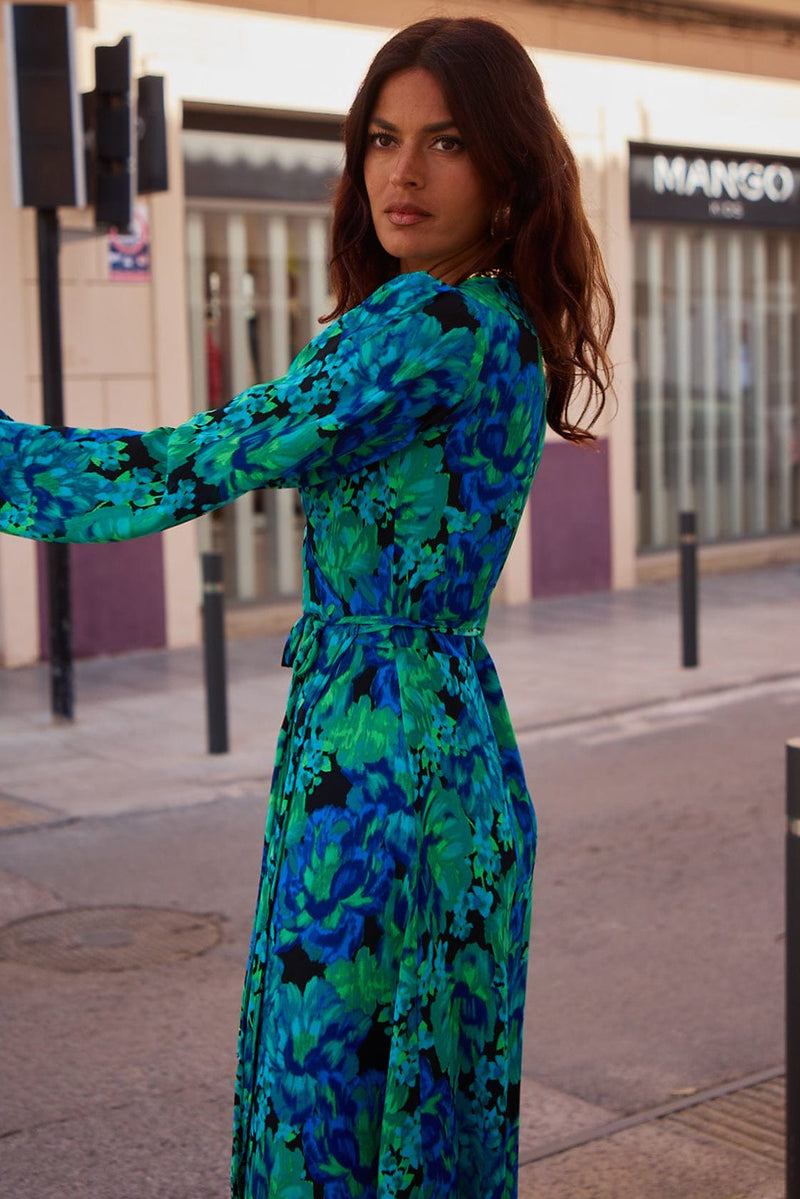 Female model is facing forward. She wears a Dancing Leopard blue and green floral wrap dress and black high heels.