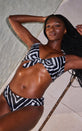 A female model lies down at the side of a pool edge. She wears Dancing Leopard monochrome bikini bottoms with a matching bikini top.
