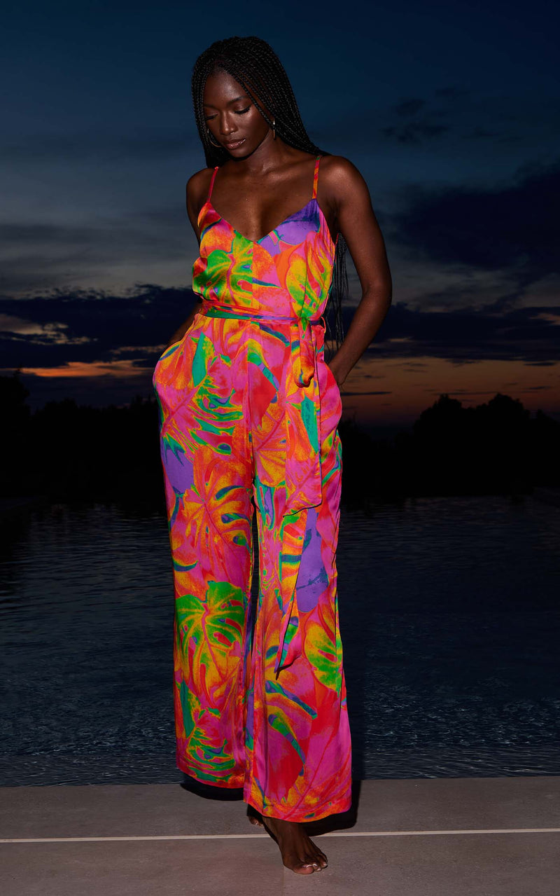 A female model faces forward in front of a pool. She wears a Dancing Leopard tropical print jumpsuit.
