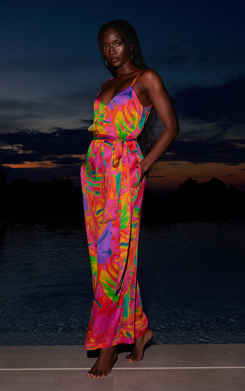 A female model faces forward in front of a pool. She wears a Dancing Leopard tropical print jumpsuit.