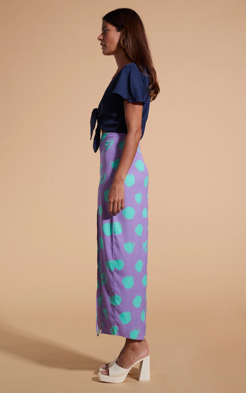 Model stands facing side-on wearing polka dot and navy maxi dress with tie-front and heels