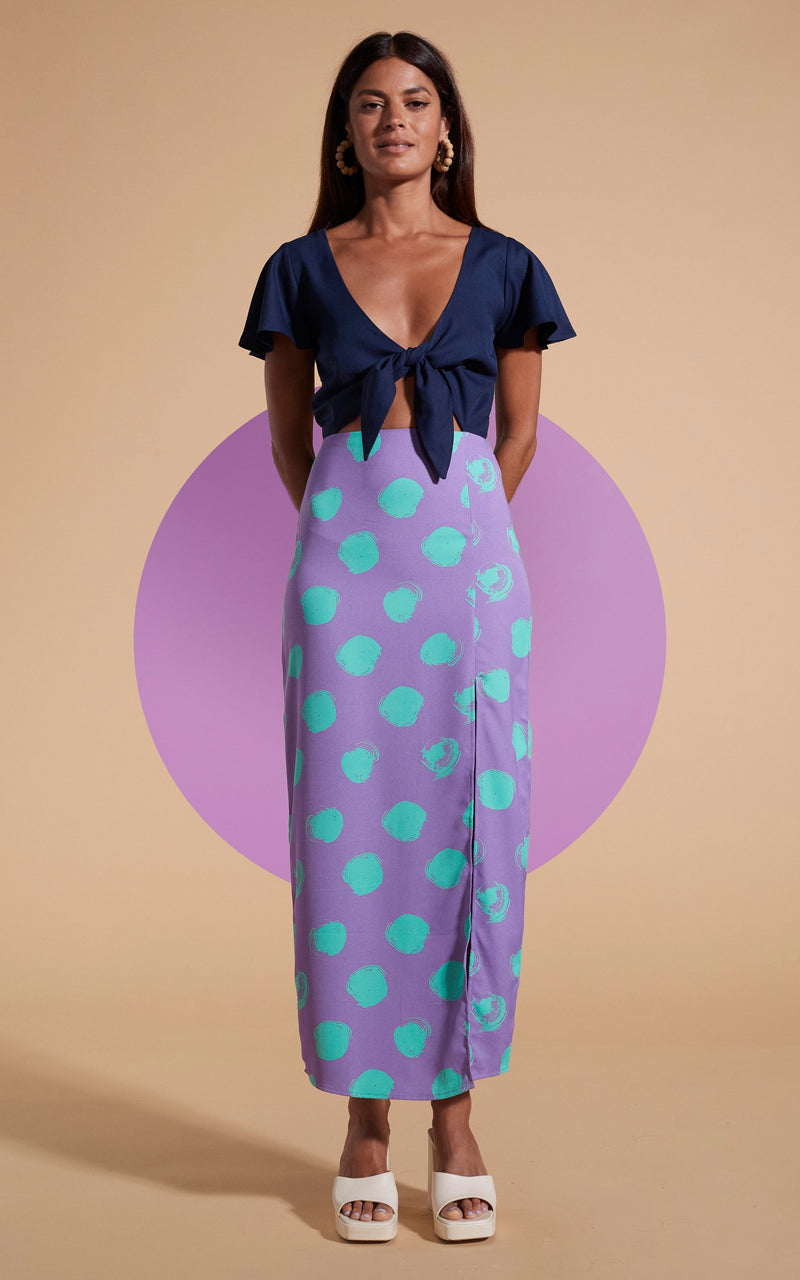 Model stands facing forwards wearing polka dot and navy maxi dress with tie-front and heels