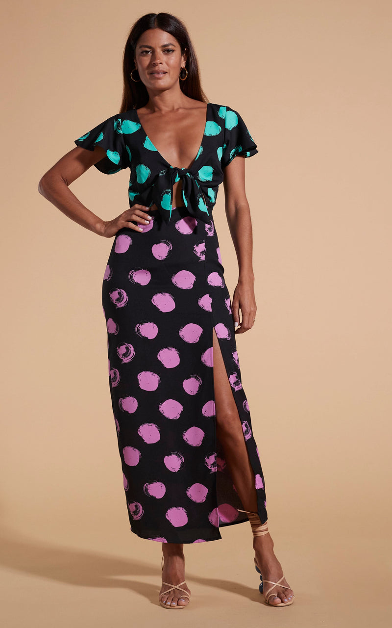 Model stands facing forwards wearing polka dot maxi dress with tie-front and heels