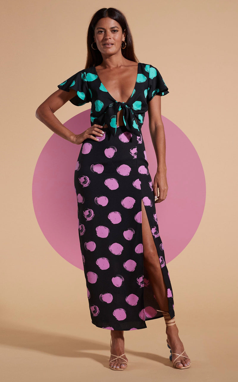 Model stands facing forwards wearing polka dot maxi dress with tie-front and heels