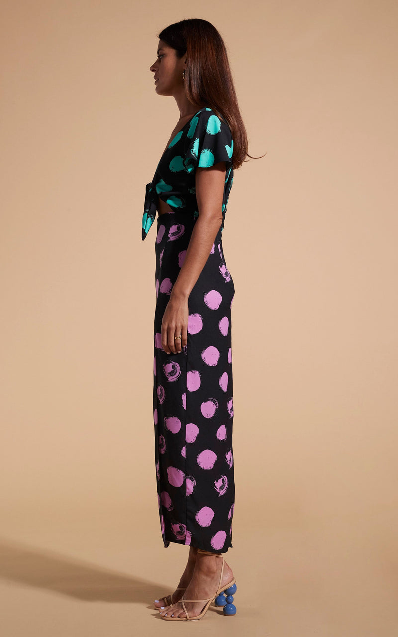 Model stands facing side-on wearing polka dot maxi dress with tie-front and heels