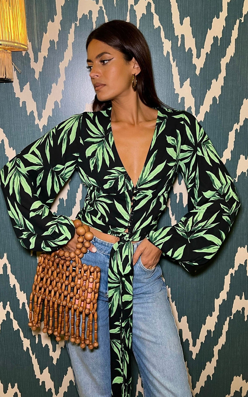 Female model is facing forwards with both hands in her pocket. She wears a Dancing Leopard tropical black and green top with blue jeans.