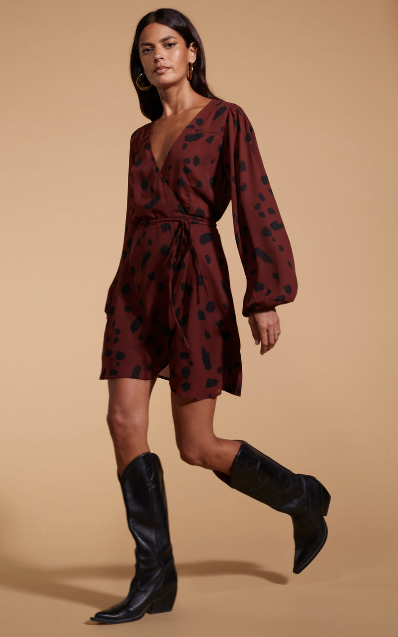 Model is facing to the side wearing a mini brown Dancing Leopard  wrap dress with black cowboy boots.