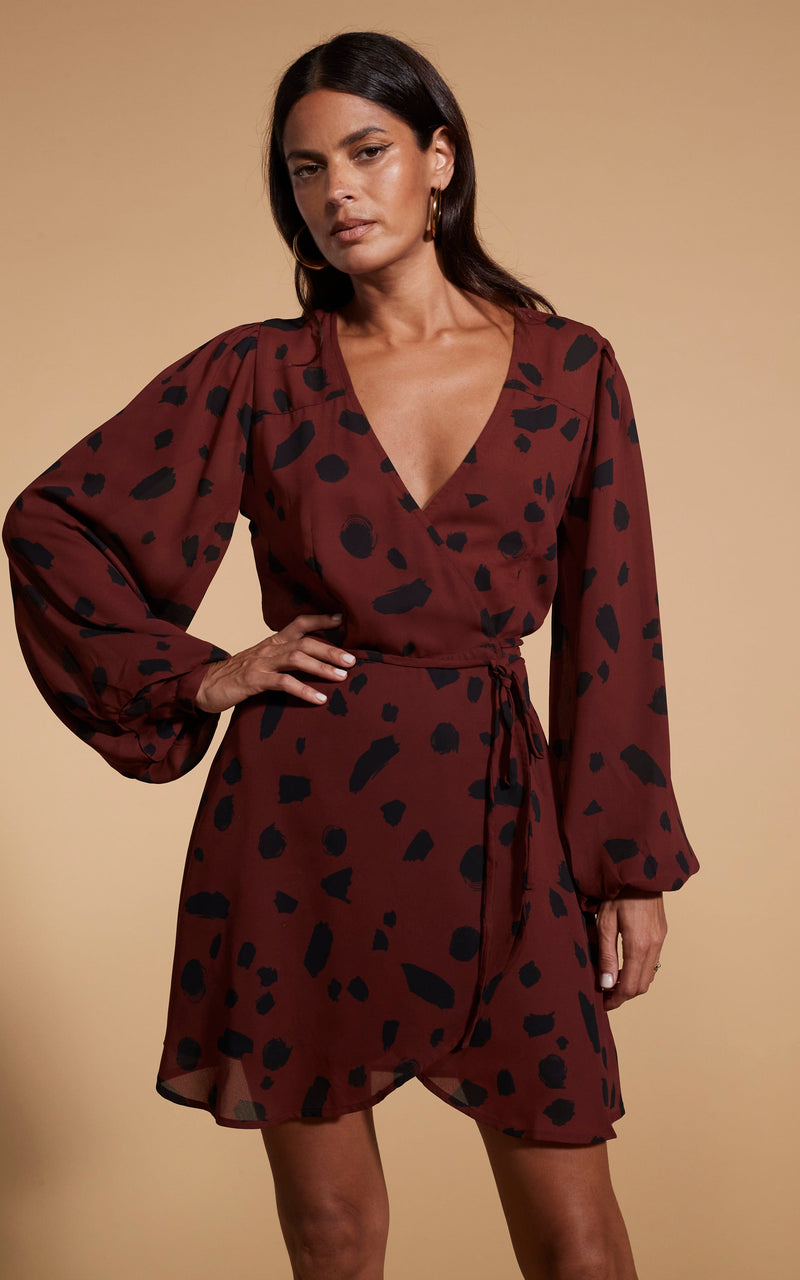 Model is facing forward wearing a mini brown Dancing Leopard  wrap dress with black cowboy boots.