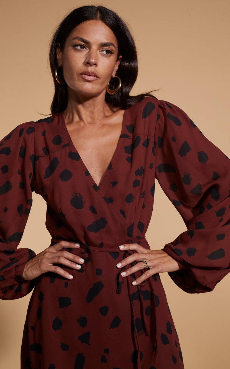 Model is facing forward wearing a mini brown Dancing Leopard  wrap dress with black cowboy boots.