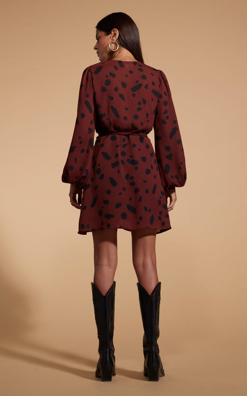 Model is facing backwards wearing a mini brown Dancing Leopard  wrap dress with black cowboy boots.