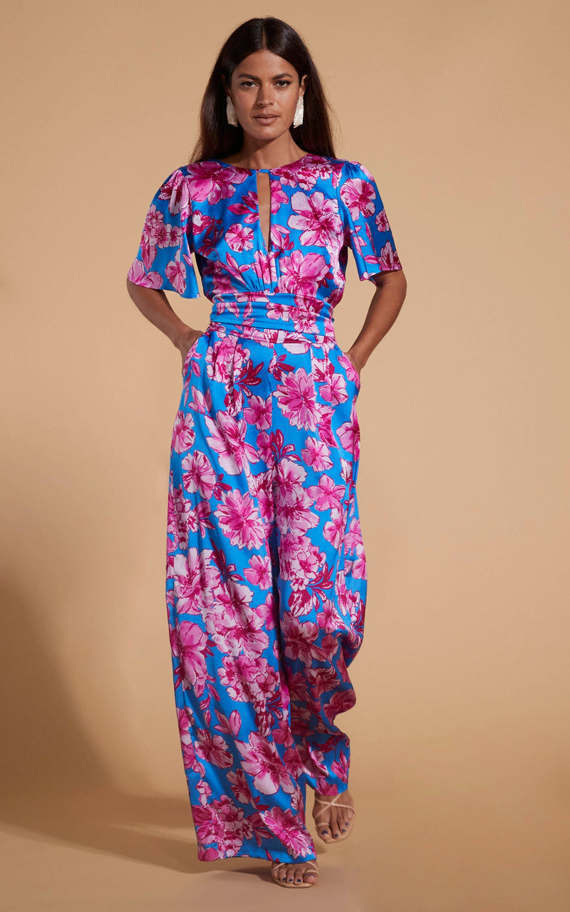 Dancing Leopard model wearing Savannah Jumpsuit In Pink On Blue Floral posed with hands in pockets