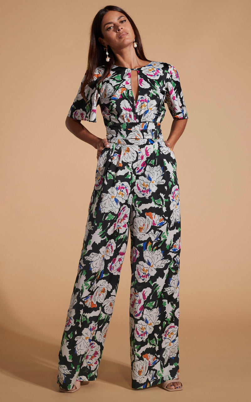 Dancing Leopard model wearing Savannah Jumpsuit In White On Black Floral posed with head tilted hands in pockets