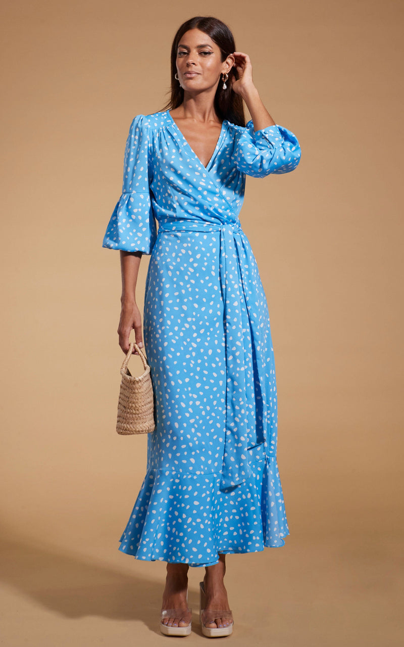 Dancing Leopard model wearing Havannah Maxi Wrap Dress in Abstract White on Blue posing with straw bag and hand on hair
