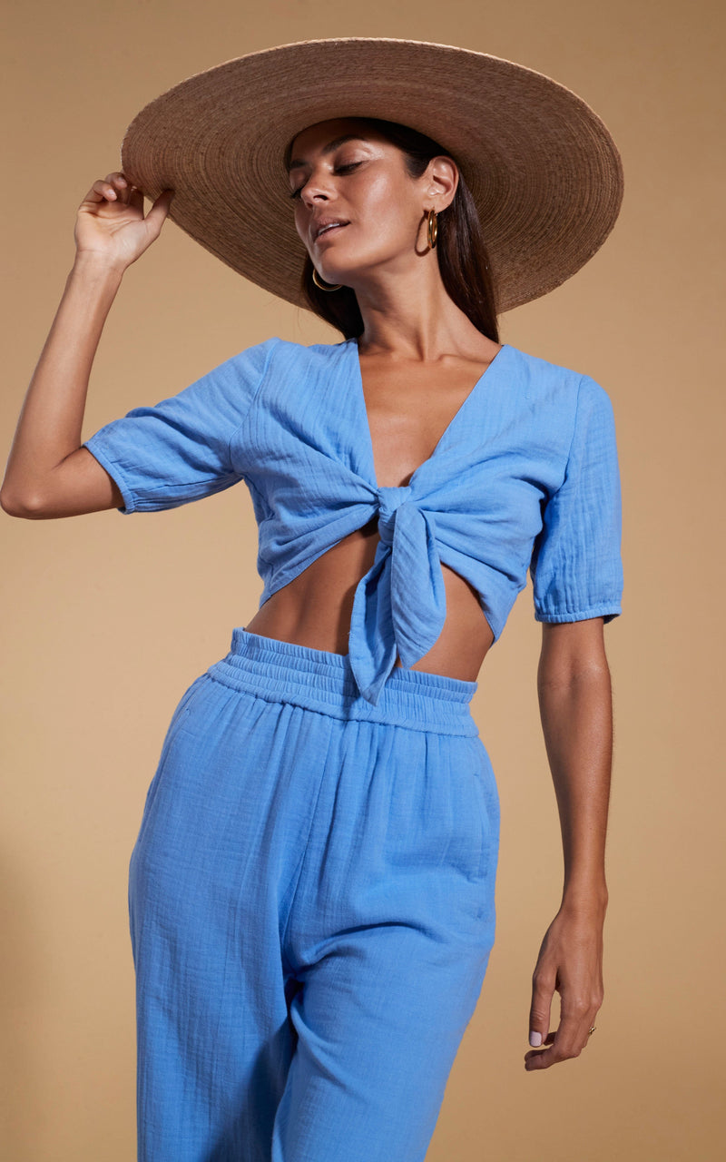 Dancing Leopard model wearing HALO Indra Tie Top in Sky Blue posed with hand on straw hat