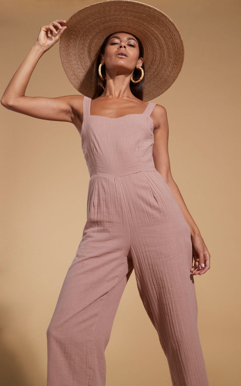 Dancing Leopard model wearing HALO Kimani Twist Back Jumpsuit in Fawn and straw hat posed with hand on hat