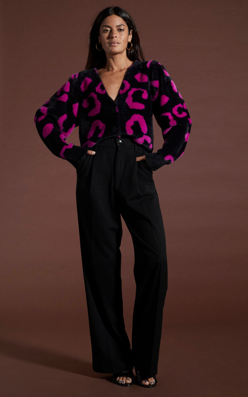 Dancing leopard model standing with hands in pocket wearing bambino cardigan in cerise on black leopard with black trousers