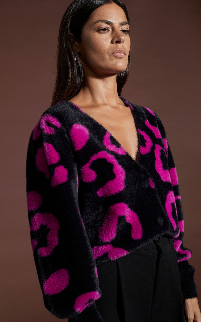 Close up of dancing leopard model standing sideways wearing Bambino cardigan in cerise on black leopard with black trousers