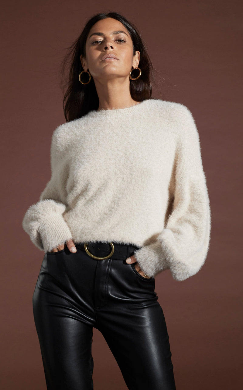 Dancing Leopard model wearing Honey Jumper in Beige and leather look trousers, posed with hands in pockets