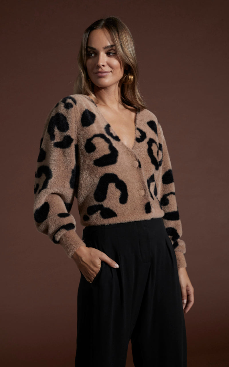 Dancing leopard model standing with one hand in pocket wearing Bambino cardigan in black on mocha leopard with black trousers