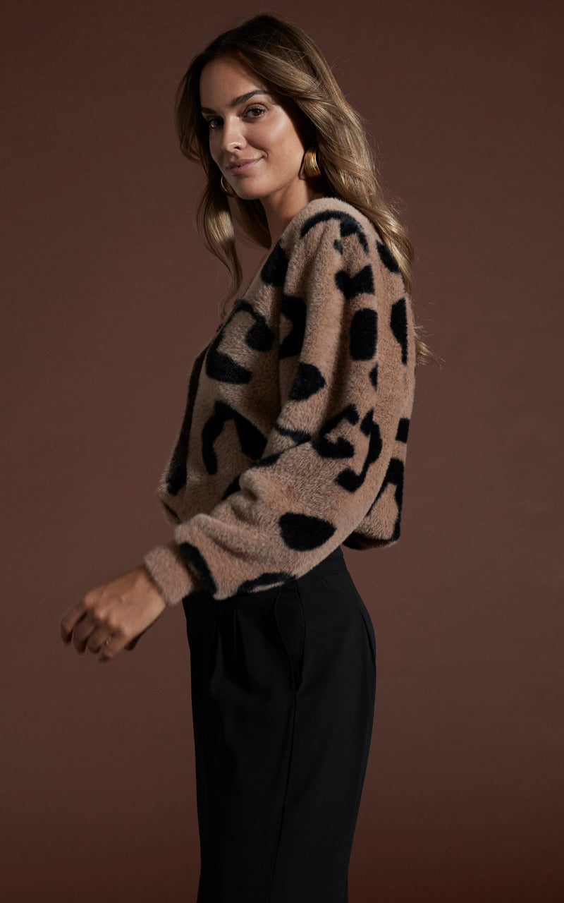 Dancing leopard model standing sideways looking at the camera wearing bambino cardigan in black on mocha leopard with black trousers