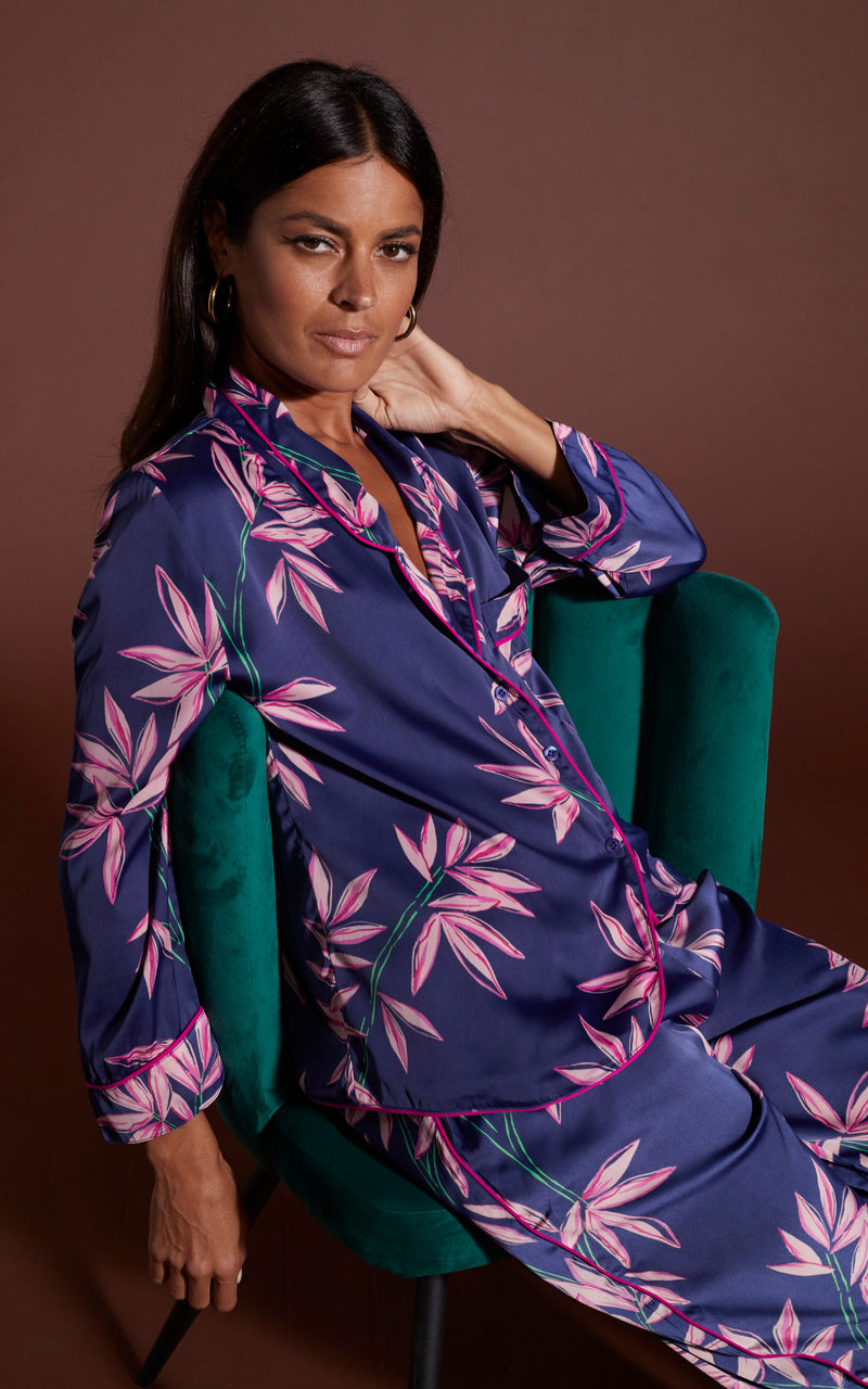 Dancing Leopard model wearing Cosmos Satin Long Leg PJ Set in Bamboo Navy Base sat relaxed in a green chair