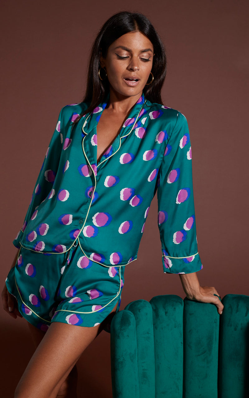 Dancing Leopard model wearing Oona Shortie PJ Set in Polka Dot Purple on Green posed stood against green chair