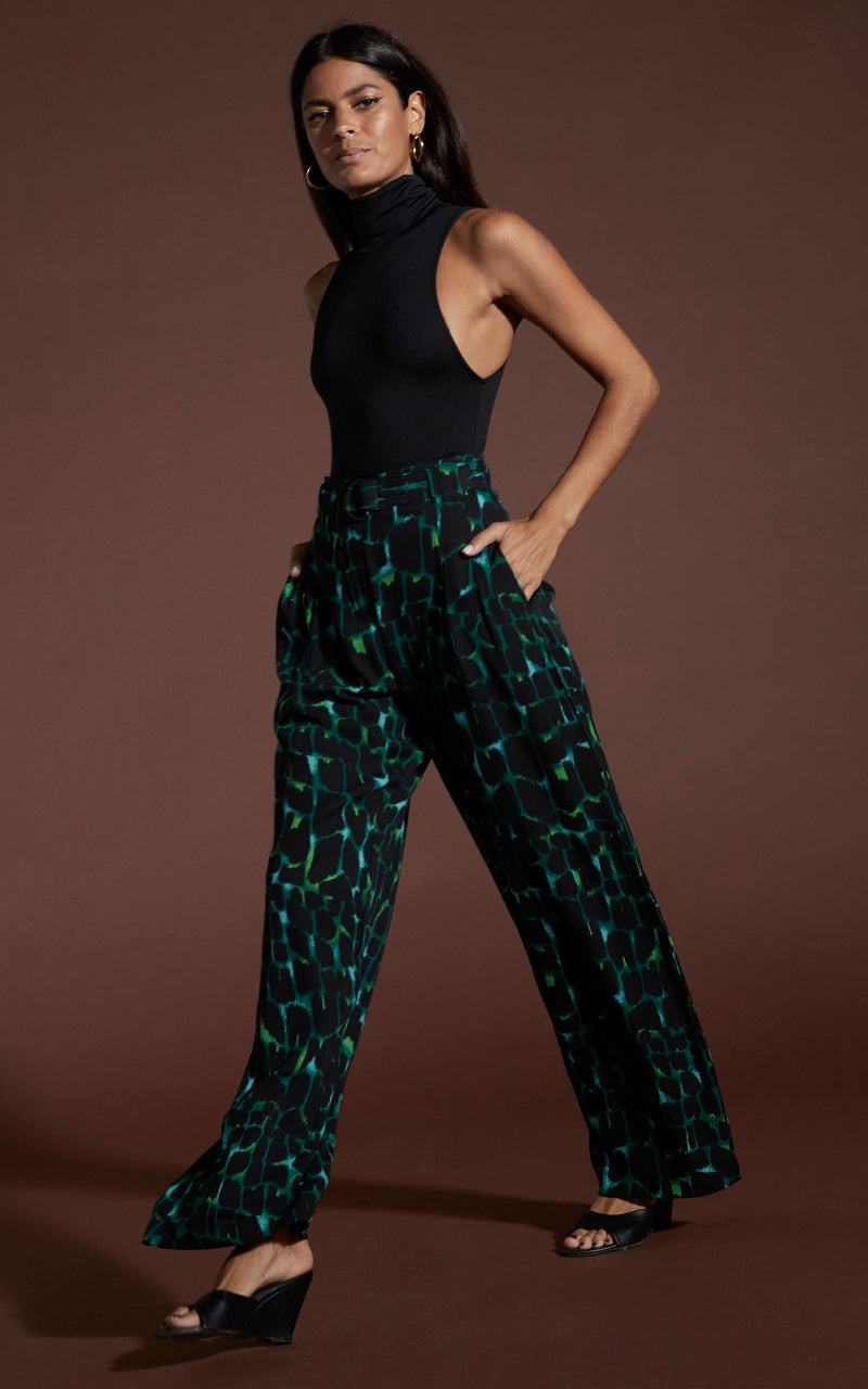 Dancing leopard model Sarah walking diagonal with hands in pockets wearing Jesse trousers in green alligator