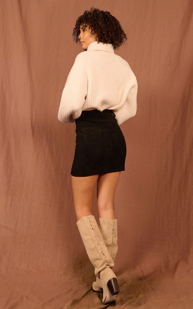 Dancing Leopard model standing with back to the camera wearing black Nikeeta skirt with cream jumper and tan knee high boots