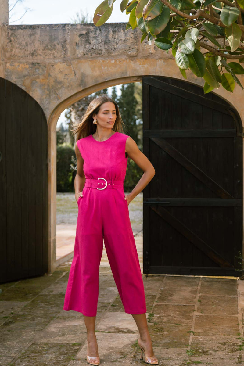 Dancing Leopard model wearing Indy Linen Jumpsuit In Raspberry - Reversible posed with hands in pockets in front of big wooden gates