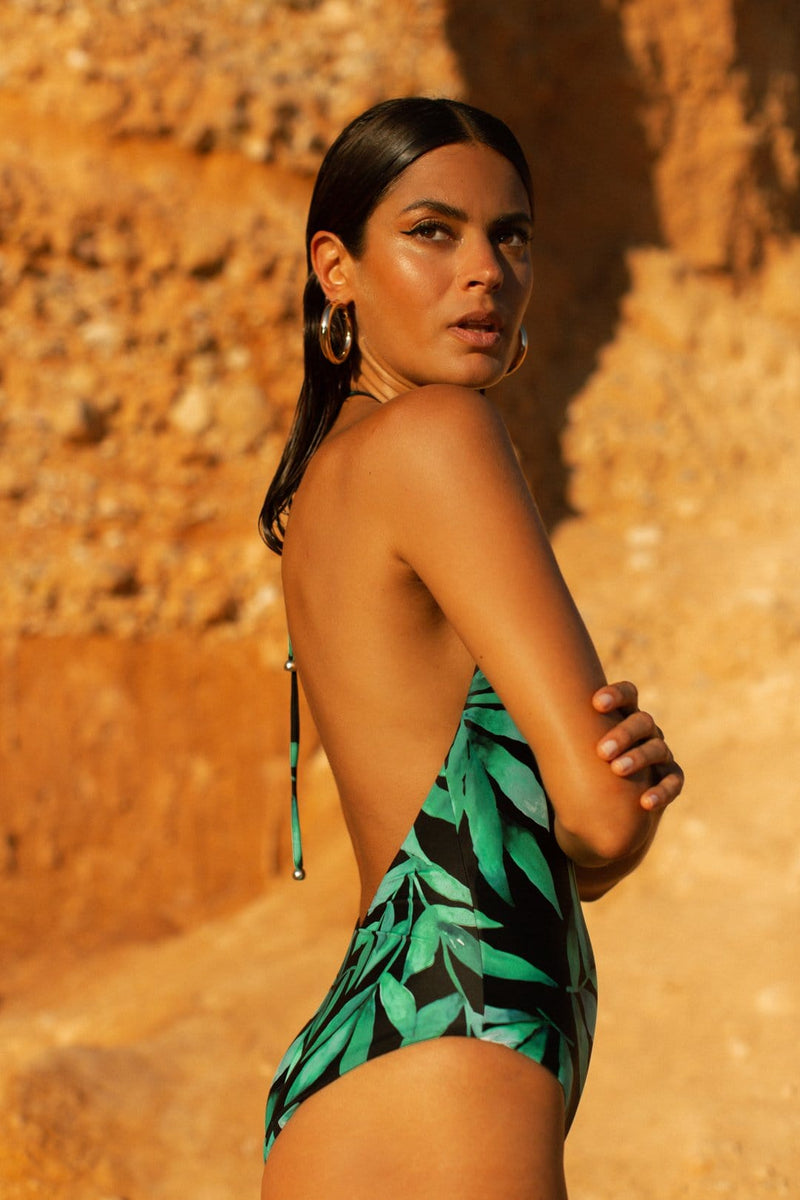 Dancing Leopard model faces side-on while standing on beach wearing tropical print high neck swimsuit and earrings