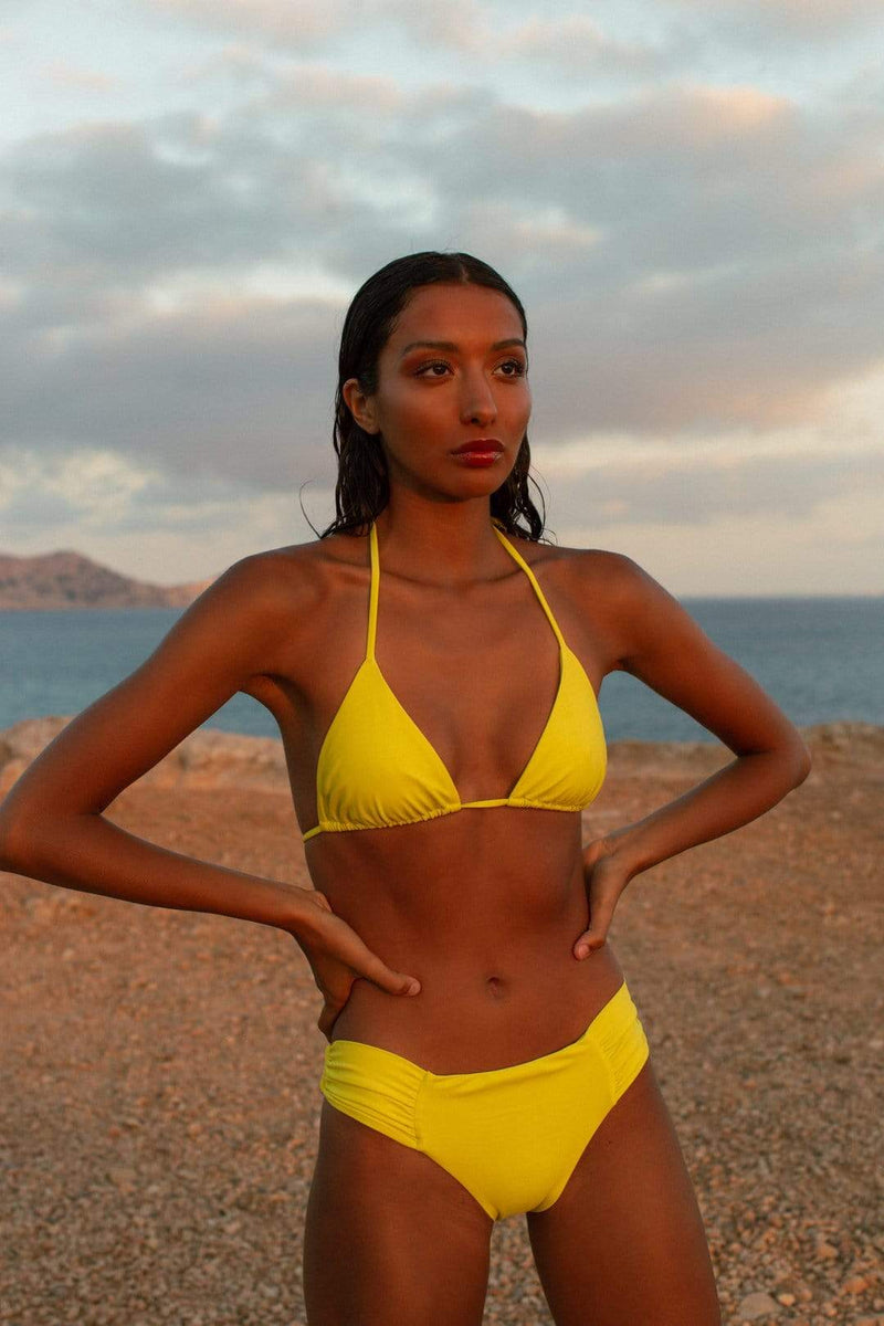 Dancing Leopard model faces forwards wearing yellow bikini top and bottoms on beach