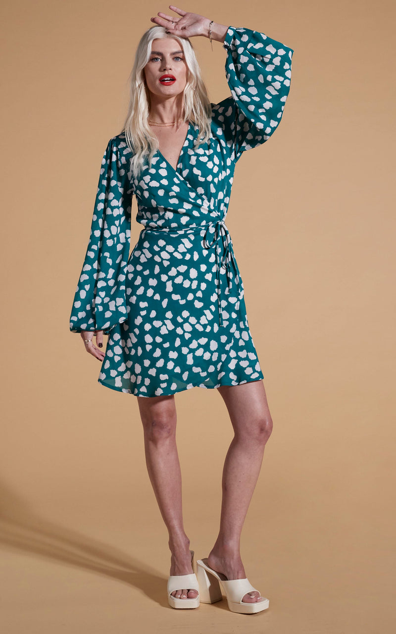 Dancing Leopard model wearing Ginger Mini Wrap Dress In White On Green Cloud posed with hand on head