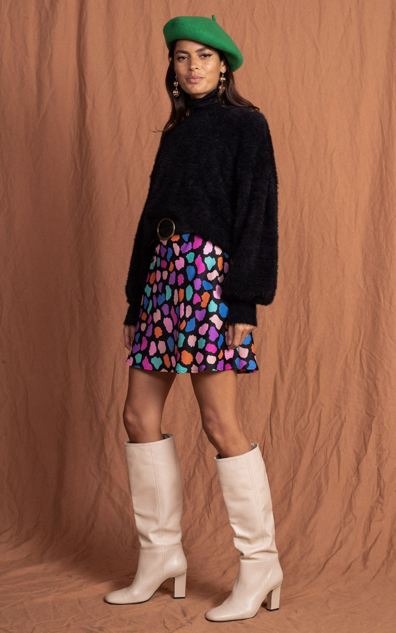 Dancing Leopard model faces sideways wearing Stevie Skirt in multi cloud with fluffy jumper, green hat and boots
