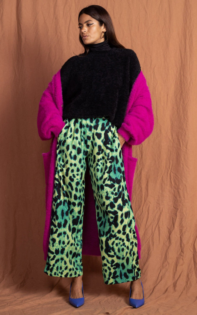 Dancing Leopard model standing forward with hands in pockets wearing lime green leopard print joey trousers with black jumper and pink cardigan