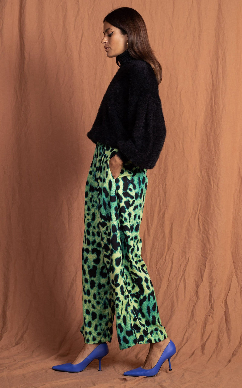 Dancing Leopard model standing sideways with hands in pockets wearing lime green leopard print joey trousers with black jumper and pink cardigan