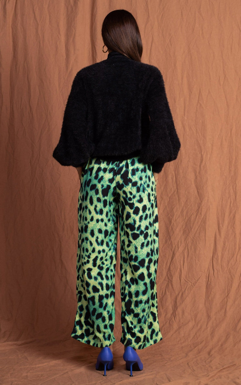 Dancing Leopard model standing back facing with hands in pockets wearing lime green leopard print joey trousers with black jumper and pink cardigan