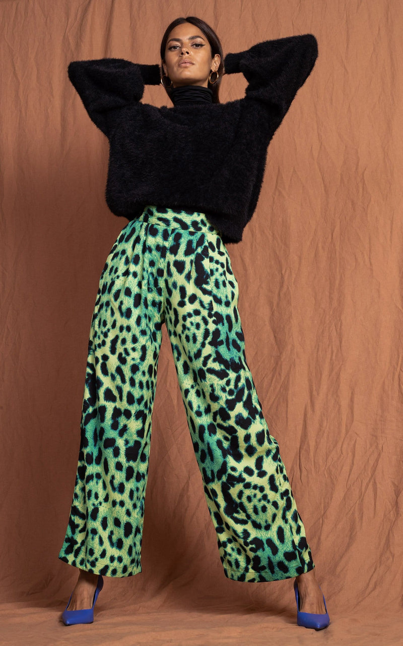 Dancing Leopard model standing forward with hands on head wearing lime green leopard print joey trousers with black jumper 