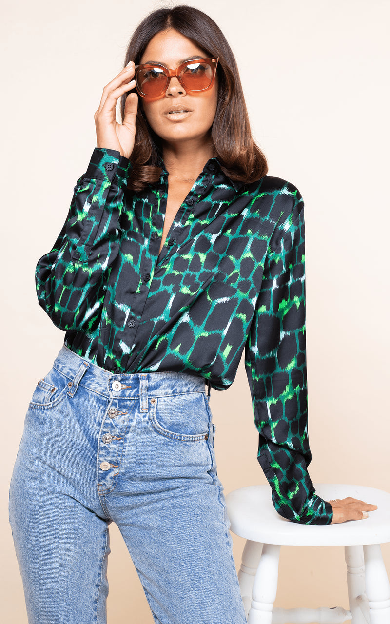 Model faces forward and leans on stool wearing Dancing Leopard San Diego Shirt in green alligator print with sun glasses and jeans