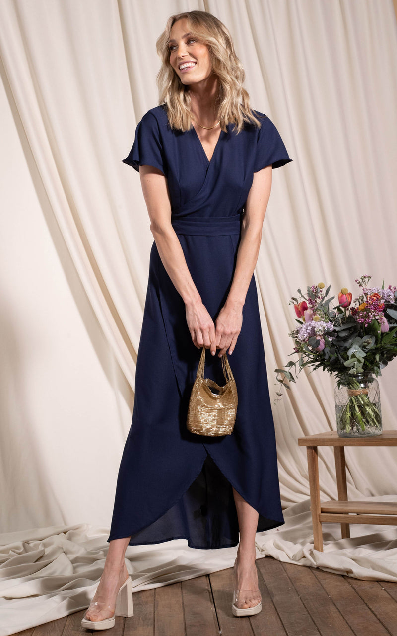 Dancing Leopard model standing holding handbag in front wearing cayenne dress in navy