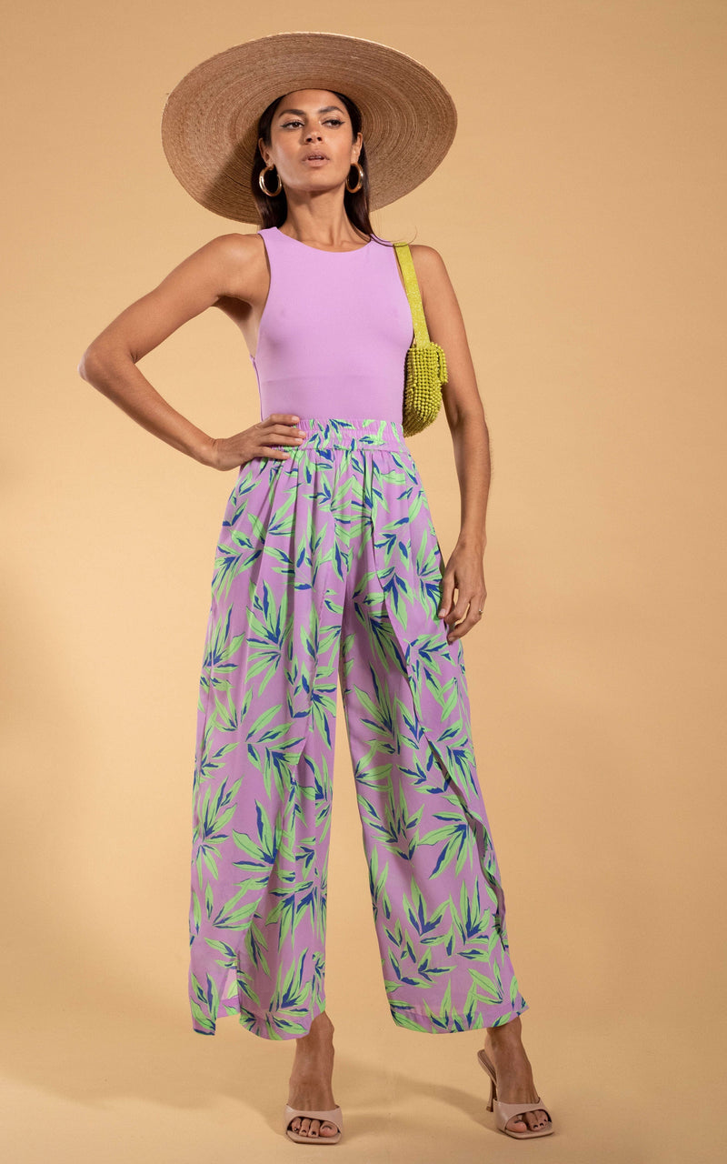 Dancing Leopard model standing with hand on hip wearing Kendari Split leg trousers in tropic mint on pint with large straw hat and yellow woven bag