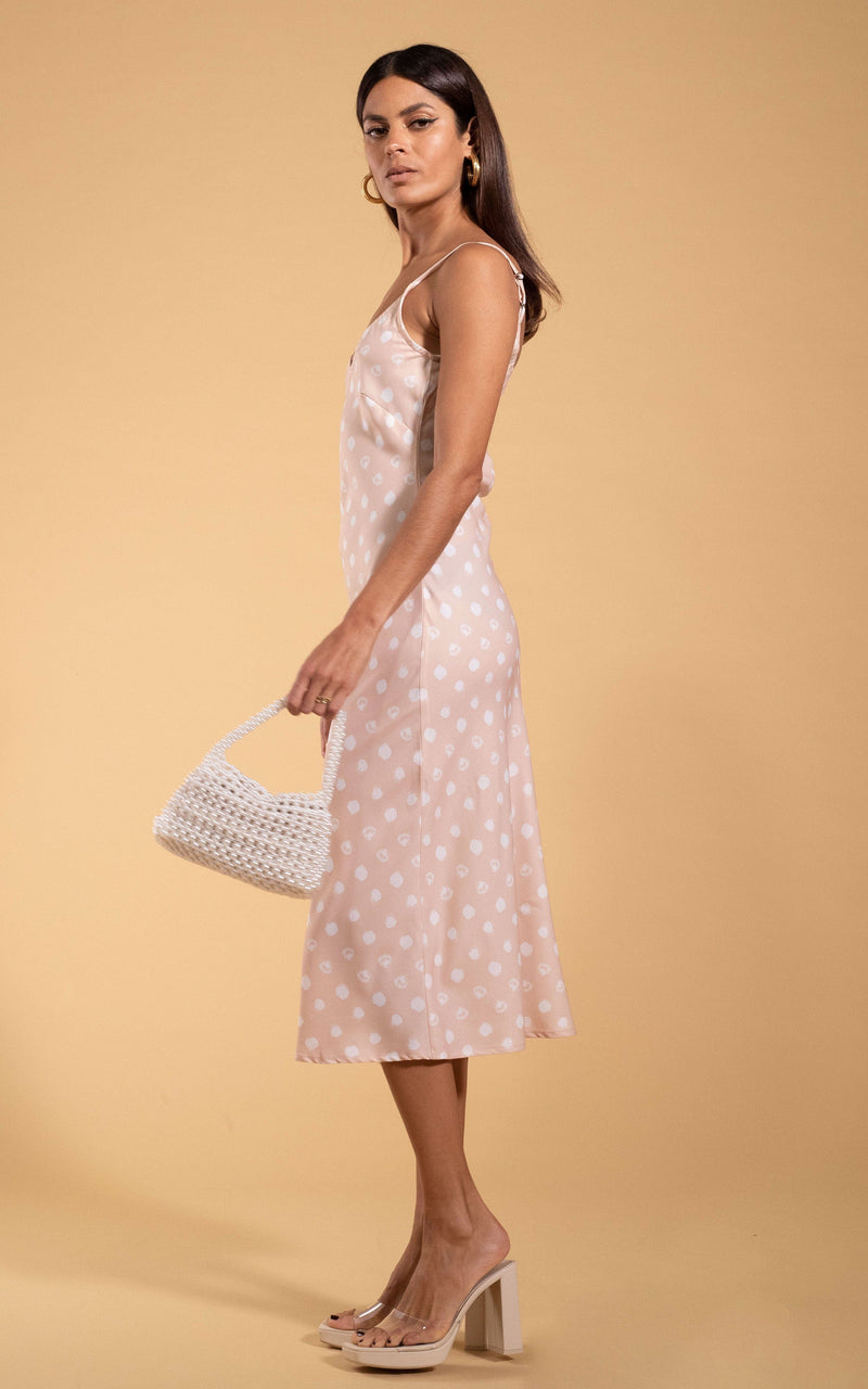 Dancing Leopard model standing sideways holding woven bag wearing Sienna midaxi dress in beige polka dot