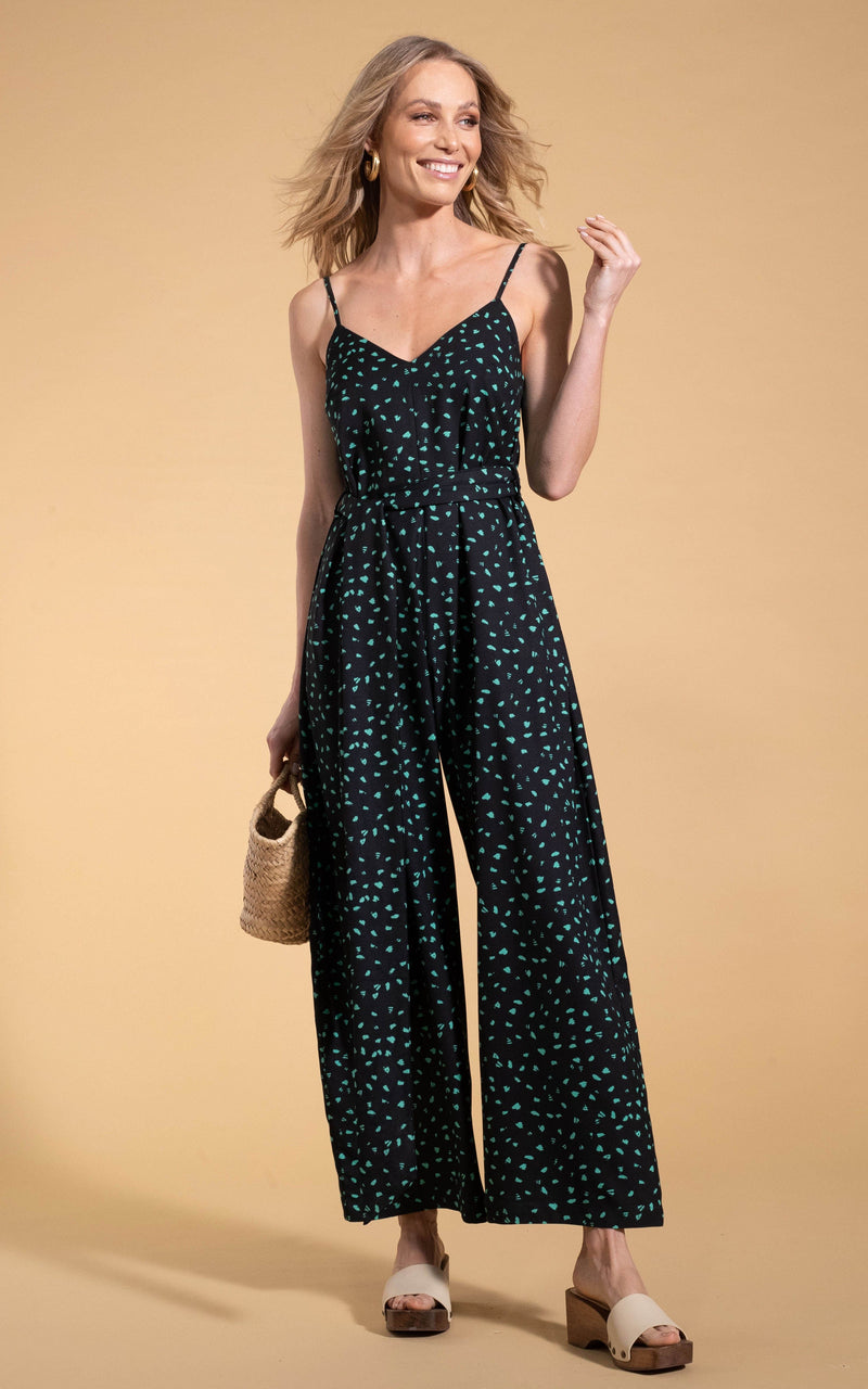Dancing Leopard model standing forwards holding bag wearing Gabriella Jumpsuit in abstract green on black