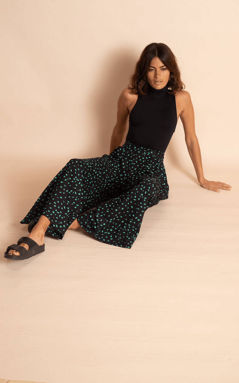 Dancing Leopard model wearing wide leg black and green dotty wide leg trousers with black bodysuit and black sandals sitting on floor