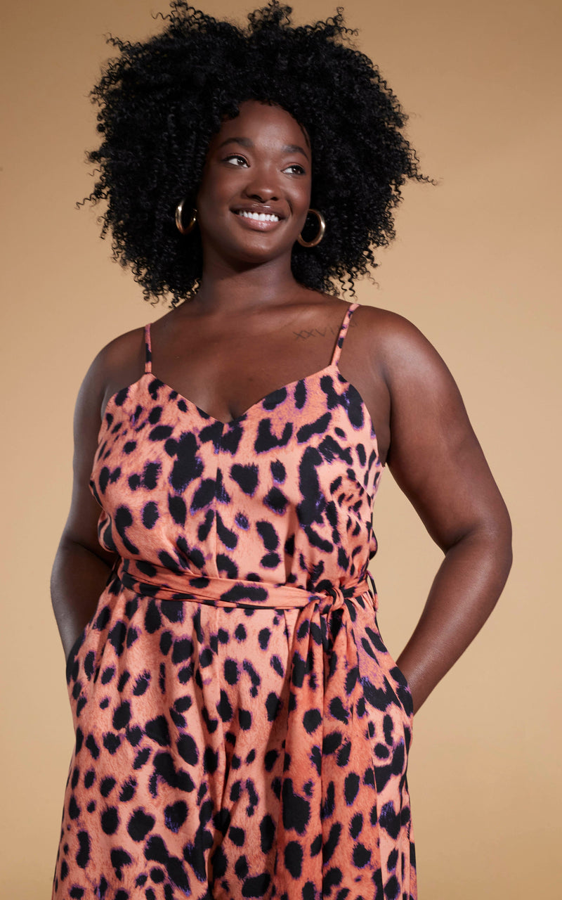 Close up of Dancing Leopard model smiling standing with hands in pockets wearing the Gabriella jumpsuit in plorange leopard 